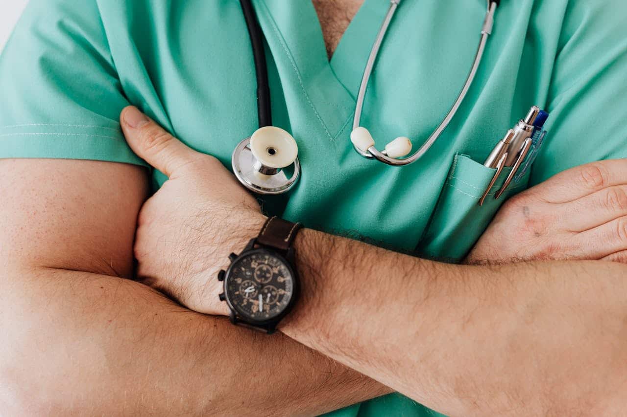 who-we-are Close-up of a healthcare professional with arms crossed wearing medical scrubs and stethoscope.