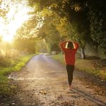Femme marchant seule sur un chemin bordé d'arbres au coucher du soleil
