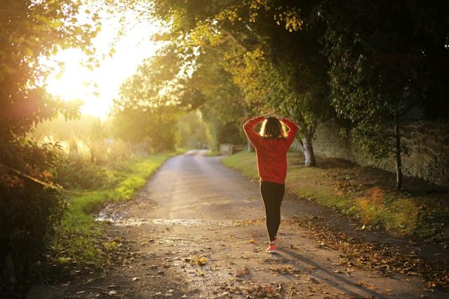 Femme marchant seule sur un chemin bordé d'arbres au coucher du soleil